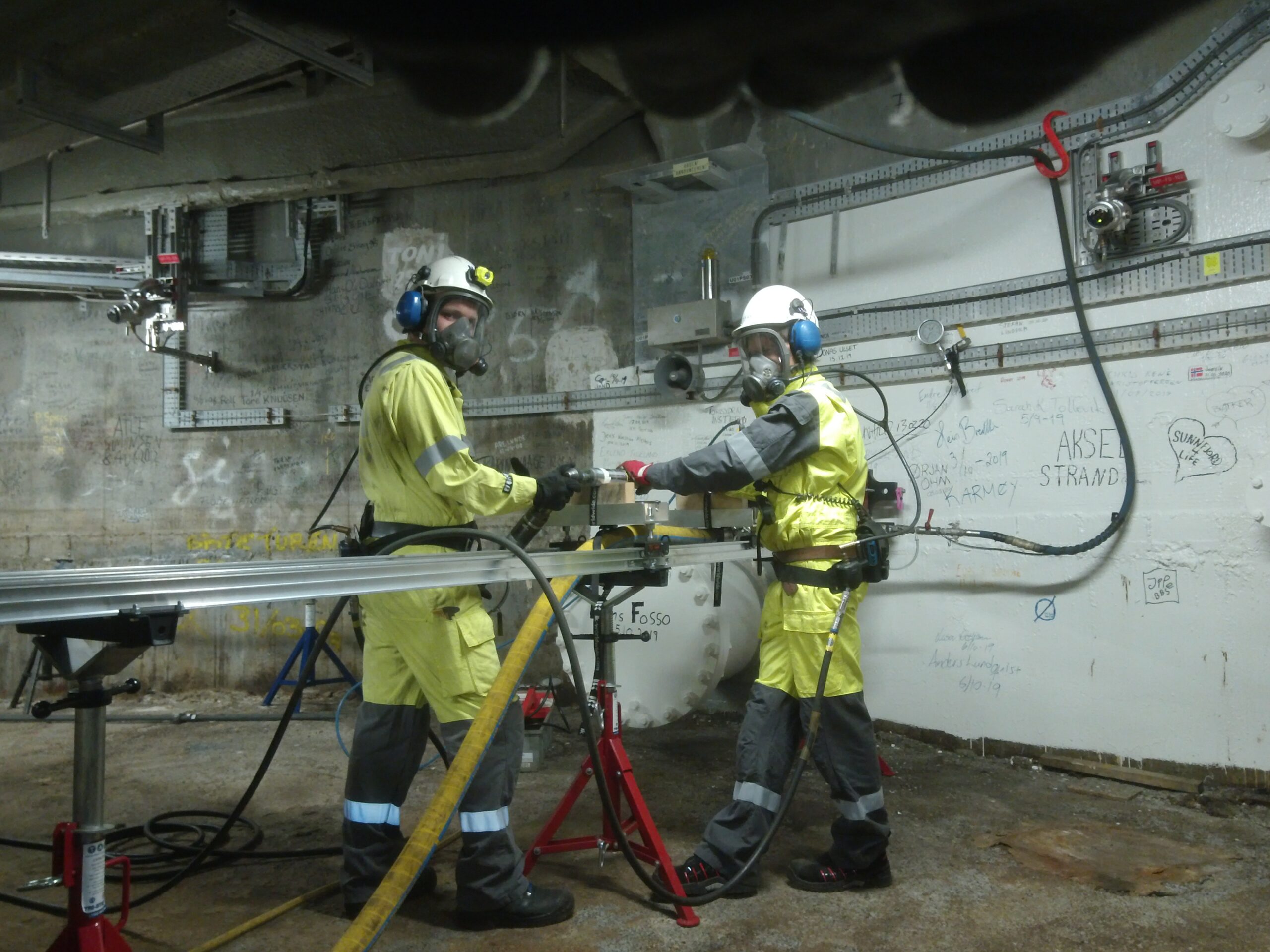 Two workers in work gear drilling through a valve