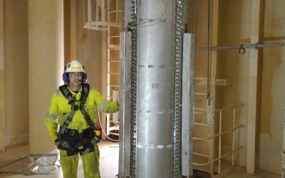 A worker standing next to a large metal pipe inside a wooden building