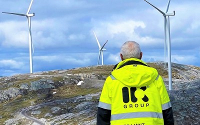 Worker standing in front of a mountainside with windmills on top and clear blue skies.