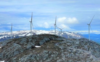 Windmills on top of a mountainside with clear blue skies and snow on top of the farthest mountain tops.