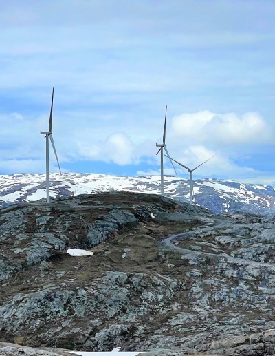 A pair of windmills on top of a mountain with clear skies and snow on the farthest mountain tops.